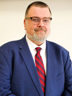 Mathias Brochhausen is a man with short dark hair and wearing a blue suit with red tie and glasses.
