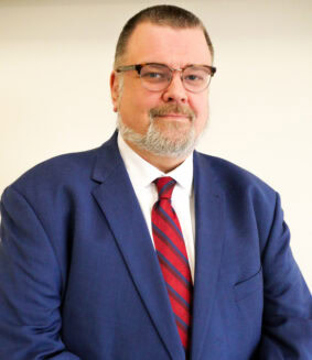 Mathias Brochhausen is a man with short dark hair and wearing a blue suit with red tie and glasses.