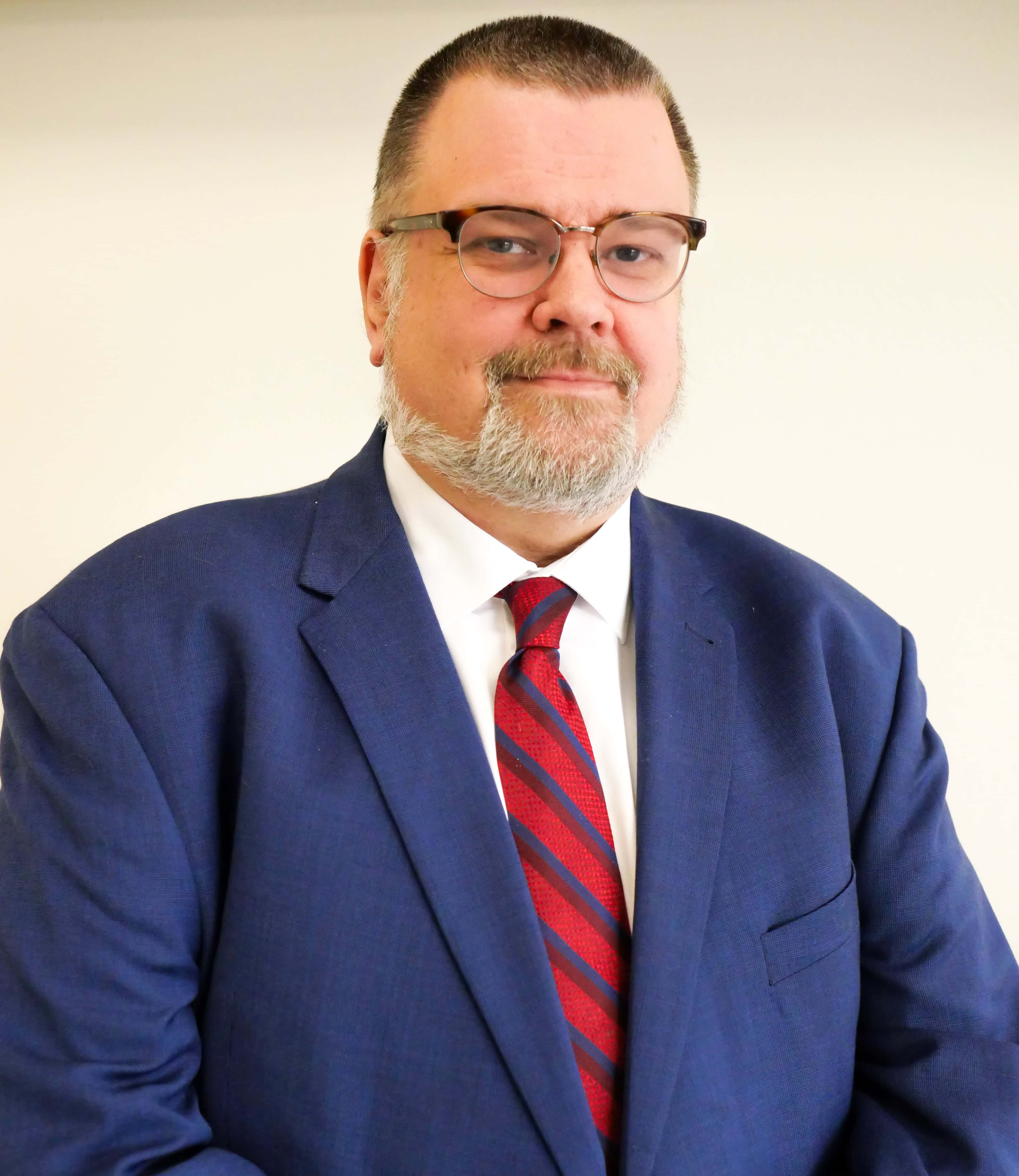 Mathias Brochhausen is a man with short dark hair and wearing a blue suit with red tie and glasses.