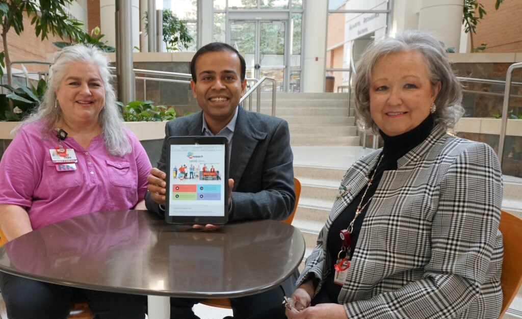 Photo caption: Nishank Jain, M.D., (center) holds an iPad displaying the ARresearch website, where more than 9,400 Arkansans have registered as potential research participants. Michelle White, RN (left), helped successfully recruit participants to Jain’s study using the ARresearch registry, and Pam Christie manages the registry for TRI.