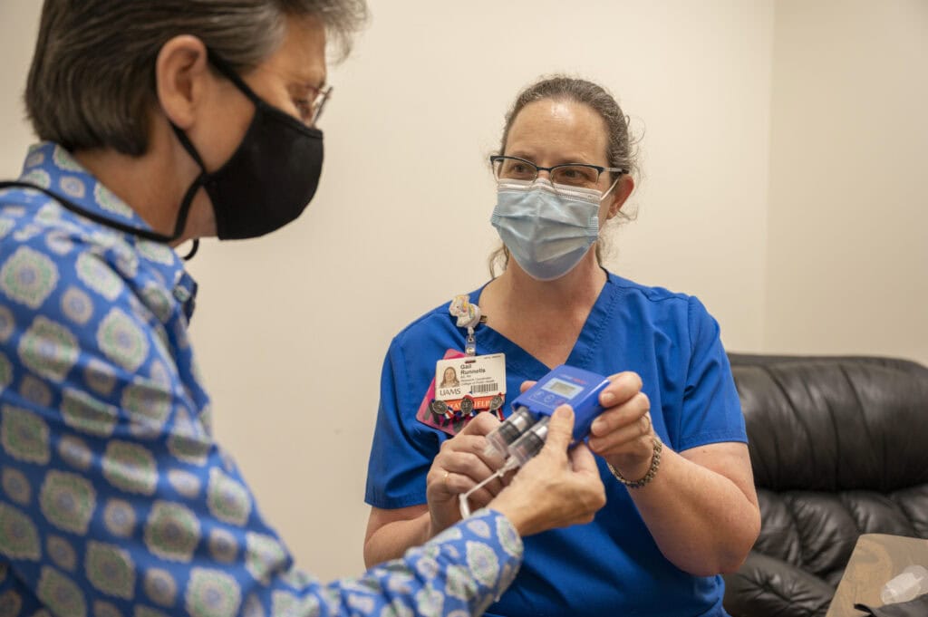 A woman nurse wearing a mask shows an info card to a male patient wearing a mask.