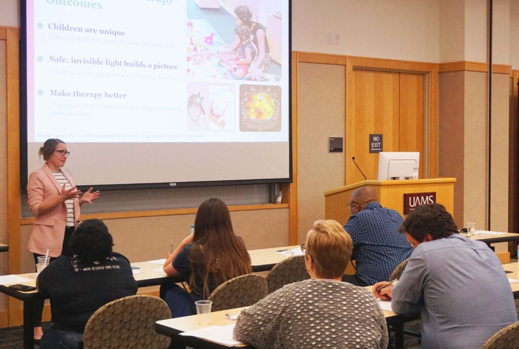 A woman stands in front of an audience with a screen behind her delivering a talk.