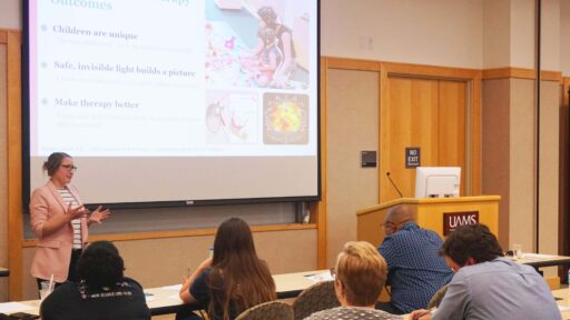 A woman delivers a talk in front of an audience with a screen behind her.