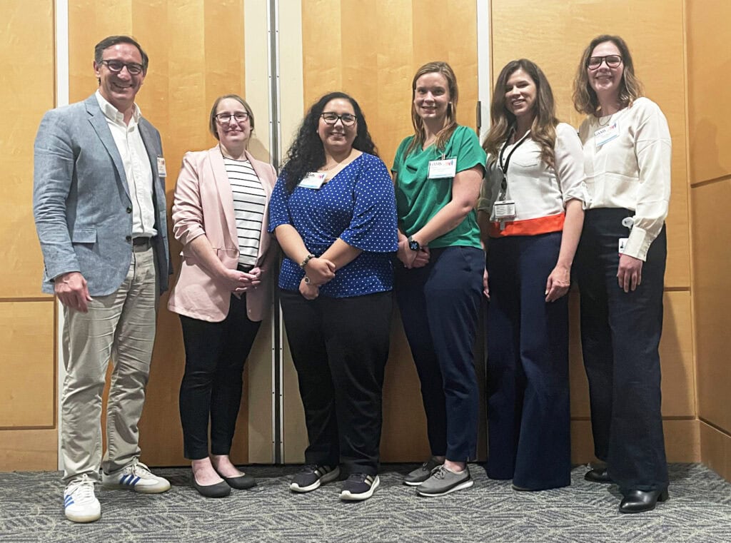 A man stands on the left with five women standing in a row going to the right.