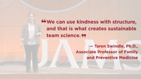 Photo of Taren Swindle on stage. She is wearing a gray jacket over a white top and black pants. Quote on image reads: “We can use kindness with structure, and that is what creates sustainable team science.”