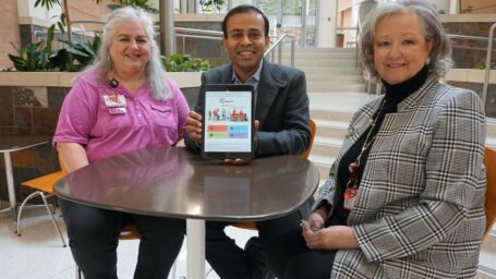 Nishank Jain, M.D., (center) holds an iPad displaying the ARresearch website, where more than 9,400 Arkansans have registered as potential research participants. Michelle White, RN (left), helped successfully recruit participants to Jain’s study using the ARresearch registry, and Pam Christie manages the registry for TRI.